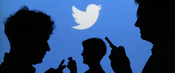 People holding mobile phones are silhouetted against a backdrop projected with the Twitter logo  in Warsaw